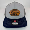 Richardson 112 patch hat in grey with charcoal mesh and navy bill, featuring a laser-engraved leather patch reading "Hoochie Daddy" on the front panel.