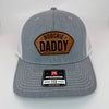 Richardson 112 patch hat in heather grey with white mesh, featuring a laser-engraved leather patch reading "Hoochie Daddy" on the front panel.