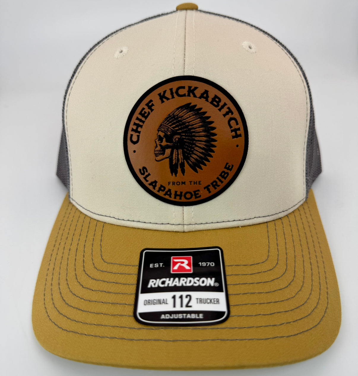 Mink Beige Richardson 112 hat with charcoal mesh back and amber accents, featuring a laser-engraved leather patch that reads “Chief Kickabitch from the Slapahoe Tribe.”