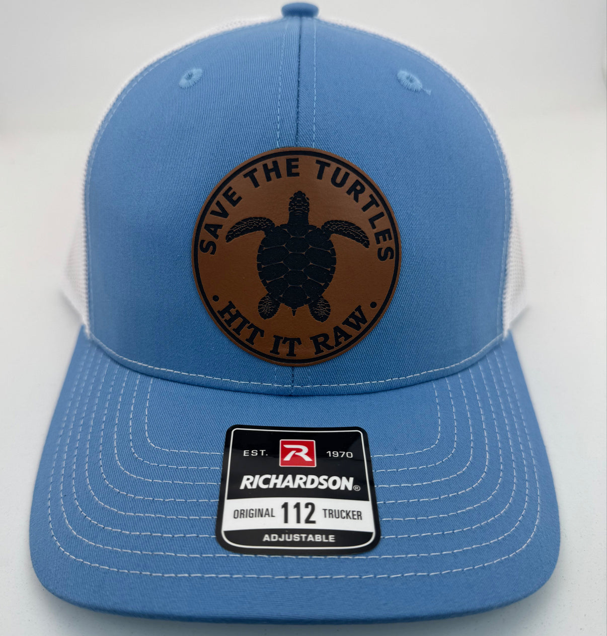 Richardson 112 trucker hat with custom laser engraved leather patch featuring Save the Turtles, Hit it Raw logo, Columbia Blue and White color scheme